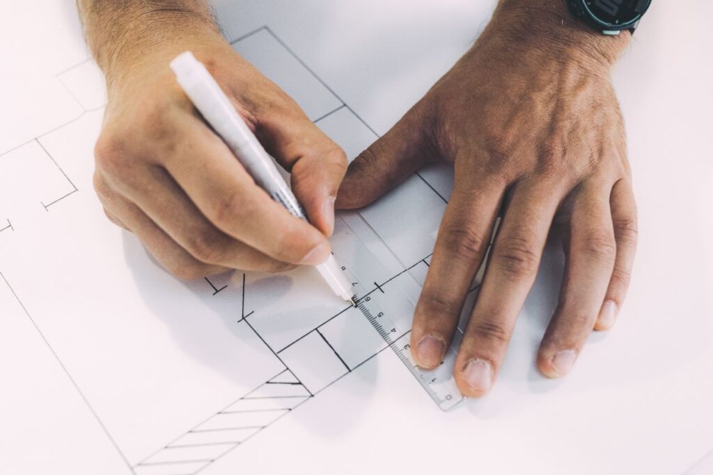Hände beim Zeichnen eines Grundrisses mit Lineal und Stift